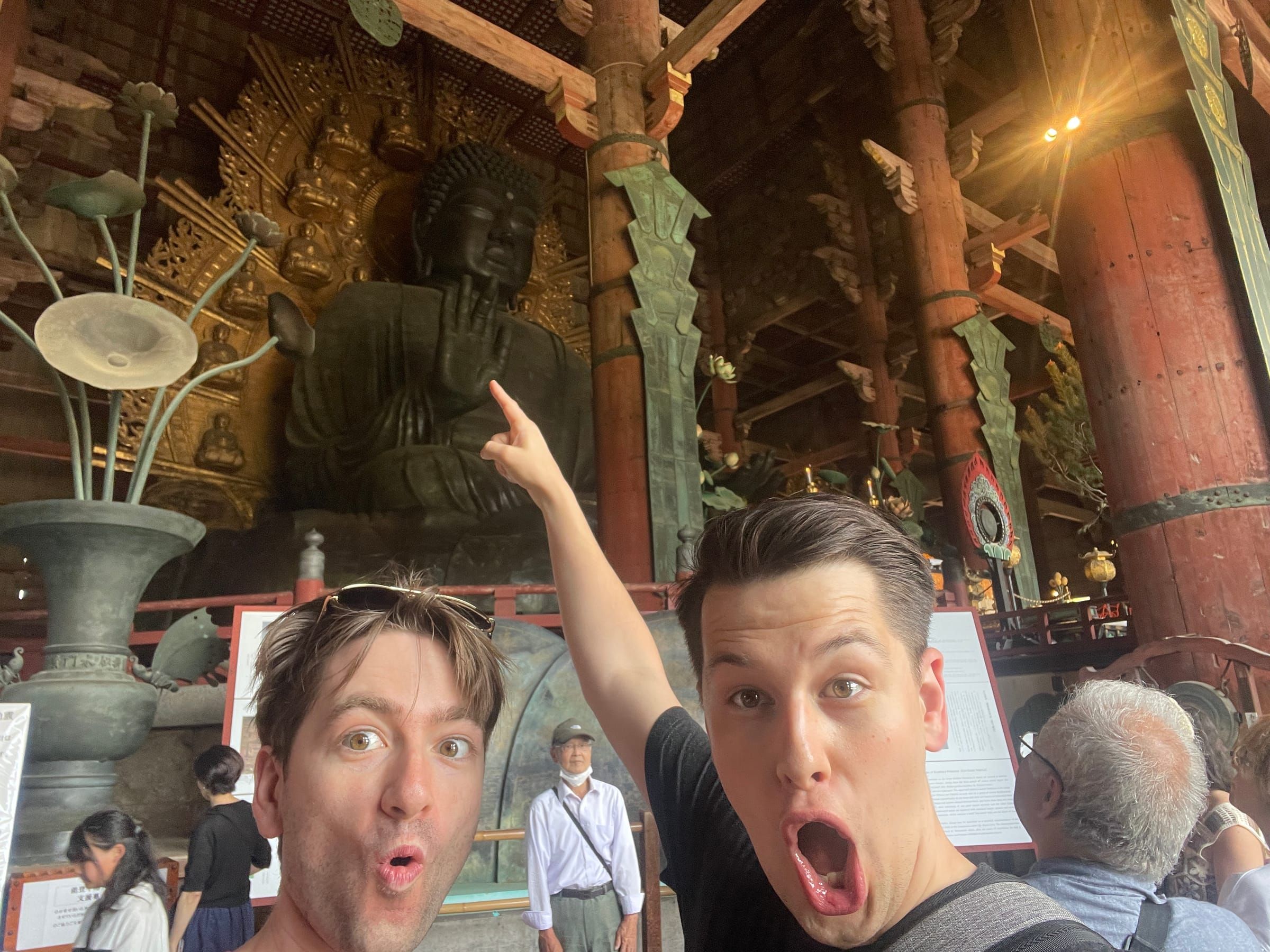 Two friends pulling surprised faces in front of a giant Buddha statue in Japan
