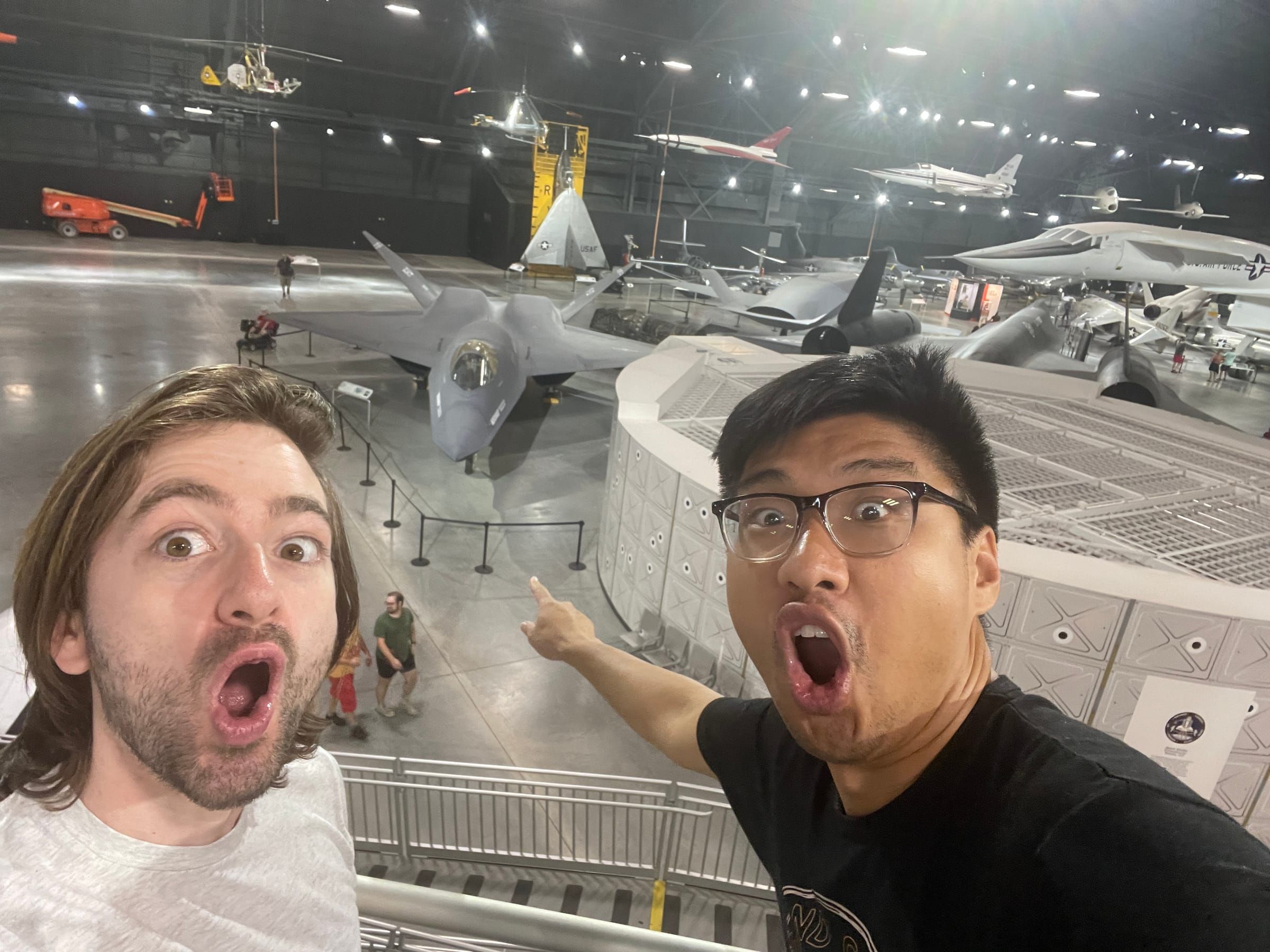 Andre and a friend pulling surprised faces above an aircraft museum hangar