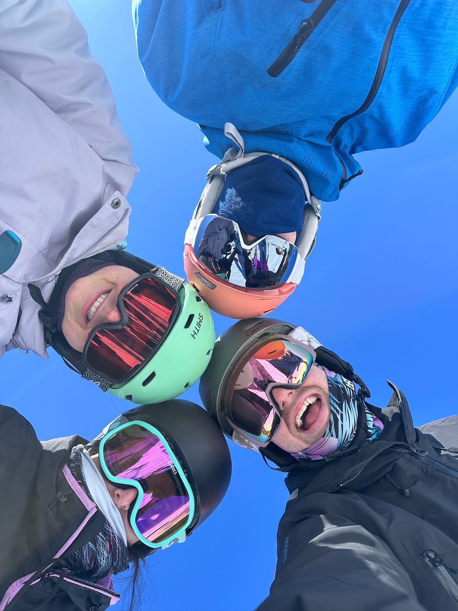Four friends in ski helmets and goggles looking down into the camera