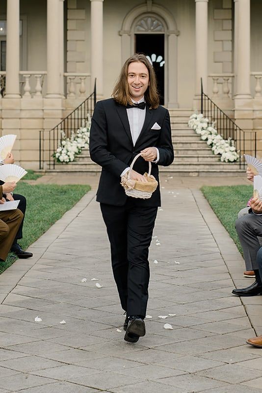 Andre walking down a wedding aisle as flower master, carrying a basket